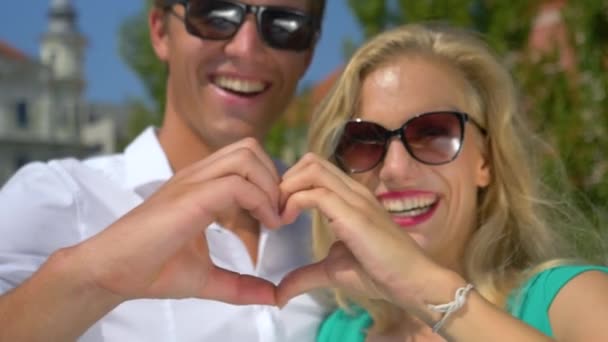 HANDHELD: Young man and his girlfriend laugh and create a heart with their hands — Stock Video