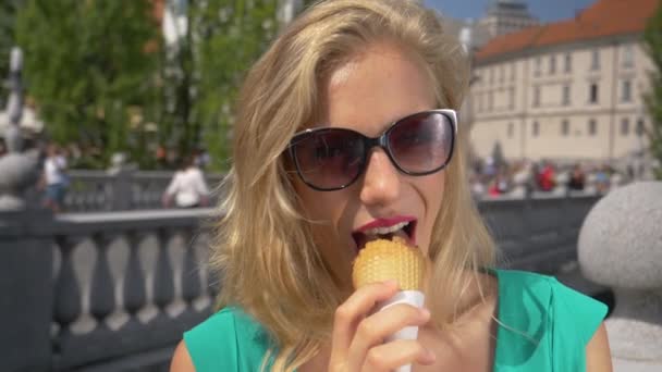 Handheld:ブロンドの女の子はリュブリャナの晴れた日にコーンからアイスクリームを食べる. — ストック動画