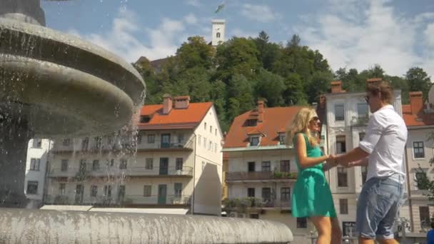 SLOW MOTION: Par som håller händer och snurrar vid en fontän på en solig dag. — Stockvideo