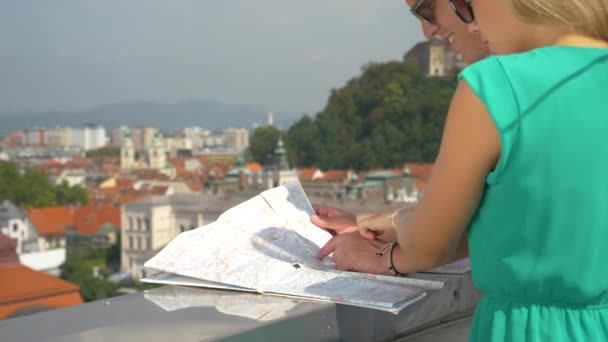 MANOS: Una joven pareja de viajeros mira un mapa y el paisaje urbano desde una azotea . — Vídeos de Stock