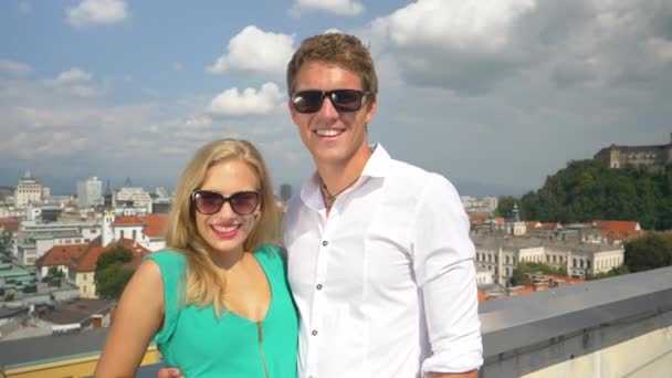 HANDHELD: Allegro coppia caucasica onde alla macchina fotografica mentre in piedi su un tetto — Video Stock
