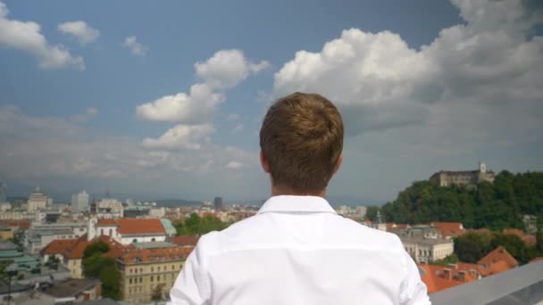 Handheld:エキサイティングなビジネスマンは屋上から美しい太陽の光の街を見る. — ストック動画