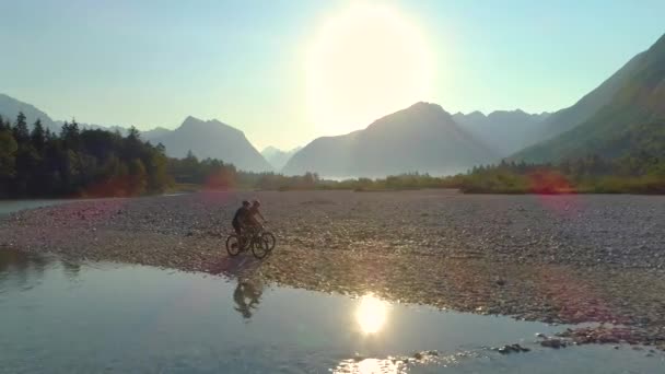 FLARE DE LA LENTE: Dos hombres disfrutan de un paseo en bicicleta escénico en el valle del río Soca iluminado por el sol. — Vídeo de stock