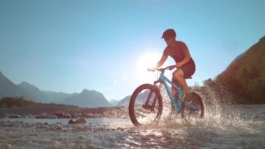 Fit adam sığ nehirde e-bisiklet sürüyor ve su sıçratıyor..