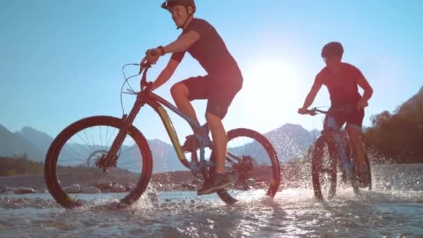 LOW ANGLE Cheerful young men having fun splashing water while riding their bikes — Stock Video