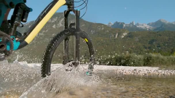 低角度：当人们骑自行车穿过一条小河时，玻璃状的水滴在镜头前飞溅. — 图库视频影像