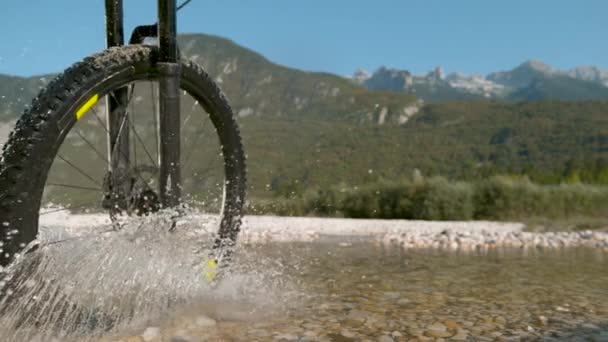 SLOW MOTION: Oigenkännlig ridning en elektrisk cykel över en grund ström. — Stockvideo