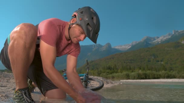 MOCIÓN LENTA: El hombre en el paseo en bicicleta salpica el refrescante agua del arroyo en su cara . — Vídeos de Stock