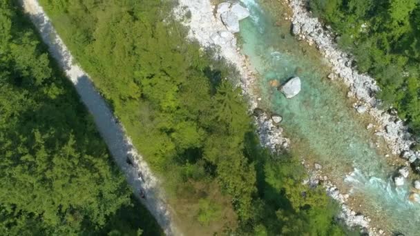 TOP DOWN: Volare sopra il fiume Soca smeraldo mentre i giovani motociclisti percorrono un sentiero vuoto . — Video Stock