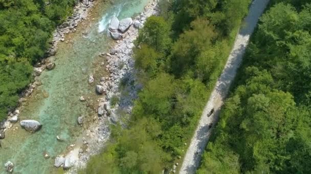 TOP DOWN: Three travelers ride bicycles along emerald Soca river on a sunny day. — Stock Video