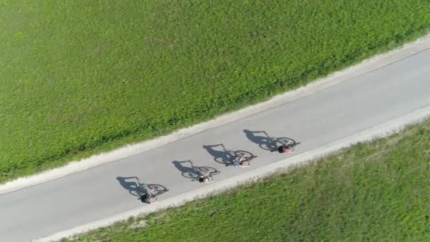 ARRIBA: Cuatro amigos montando bicicletas proyectando sombras en el camino de asfalto vacío. — Vídeos de Stock