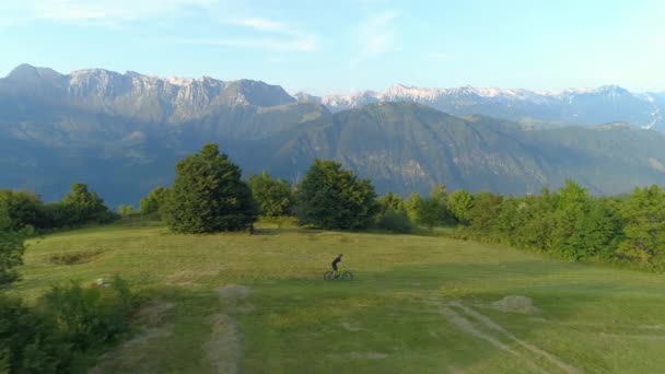 空気:彼はウサギのホップを行うように男は牧草地の間で自転車に乗るに沿って飛ぶ. — ストック動画