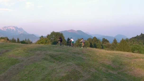 Mannen och kvinnan på cyklar trampar uppför en gräsbevuxen kulle en solig sommardag.. — Stockvideo