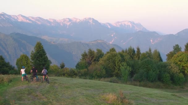 AERIAL: Los turistas jóvenes en ebikes miran alrededor de la naturaleza escénica de la tarde del verano. — Vídeos de Stock