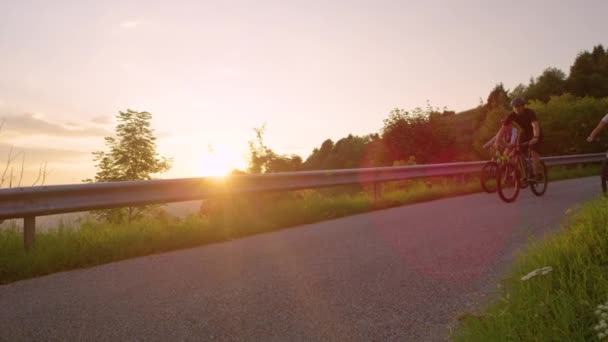 LENS FLARE: Os raios de sol da manhã brilham sobre os ciclistas de montanha descendo pela estrada . — Vídeo de Stock