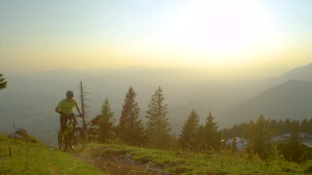 LOW ANGLE: Actieve mannelijke toerist pedalen een elektrische fiets bergop bij zonsopgang. — Stockvideo