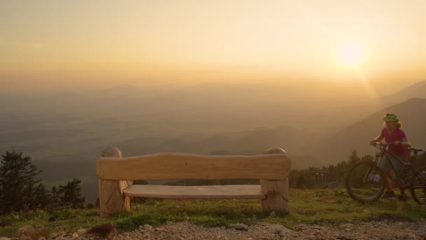 SLOW MOTION: Two mountain bikers walk with their bicycles up to a wooden bench. — Stock Video