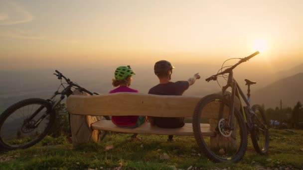 SLOW MOTION Ποδήλατο βουνού αναβάτες κάθονται σε ένα ξύλινο πάγκο και παρατηρούν το τοπίο — Αρχείο Βίντεο