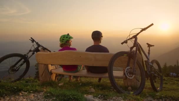 LENS FLARE: Jovens motociclistas sentam-se em um banco e punho solto após um passeio ao pôr do sol. — Vídeo de Stock