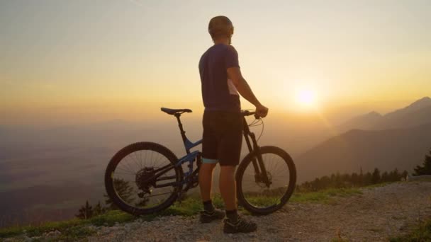 LENS FLARE: Männlicher Mountainbiker beobachtet nach erfolgreicher Fahrt den Sonnenuntergang. — Stockvideo