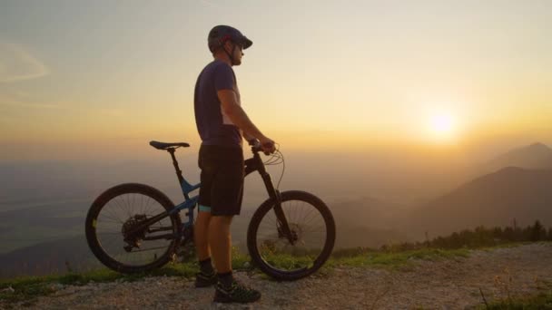 SOL FLARE El hombre se para junto a su bicicleta de montaña mientras observa la naturaleza iluminada por el sol — Vídeos de Stock
