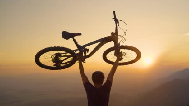 FLARE DE LA LENTE: El hombre excitado levanta su bicicleta por encima de su cabeza después de un divertido paseo en bicicleta. — Vídeo de stock