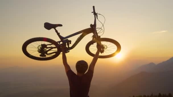 CLOSE UP Man tilt zijn fiets boven het hoofd bij zonsondergang na een mountainbiketocht — Stockvideo