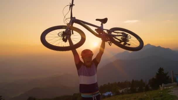 SUN FLARE: Happy man shouts while holding his bike above his head at sunset. — Stock Video