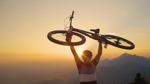 Утренние лучи солнца сияют на взволнованного человека, поднимающего свой велосипед над головой. — стоковое видео