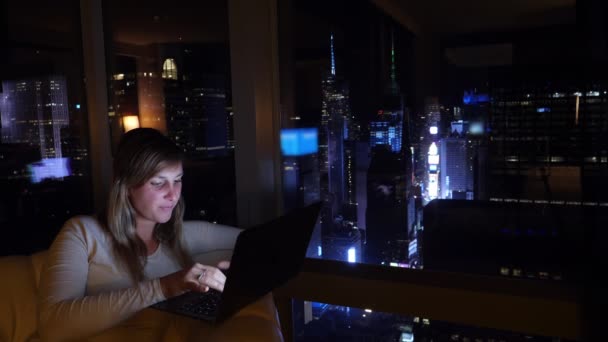 CLOSE UP: Женщина в командировке сидит в гостиничном номере с видом на Нью-Йорк ночью. — стоковое видео