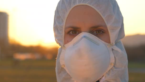 ПОРТРАЙТ: Женщина-врач в маске и костюме стоит на улице на закате — стоковое видео