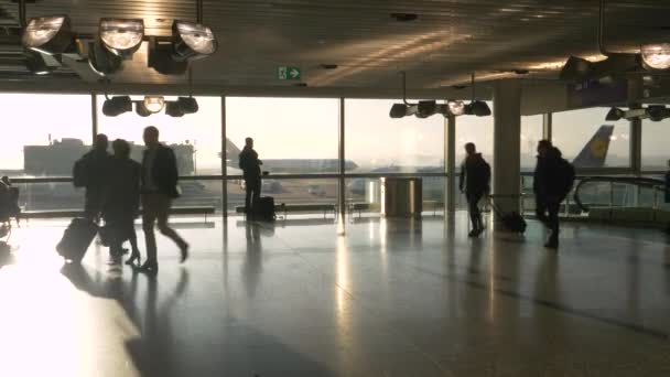 SILHOUETTE: Podróżujący śpieszą się po lotnisku, jak Lufthansa taksówki samolotowe wzdłuż pasa startowego — Wideo stockowe