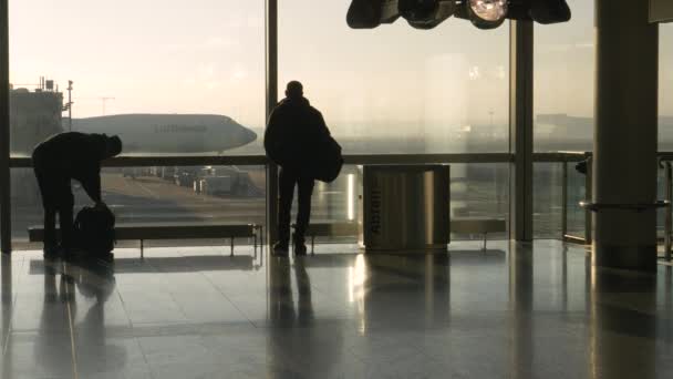 SILHOUETTE: Turista observa a pista e aviões como outros viajantes correm por — Vídeo de Stock