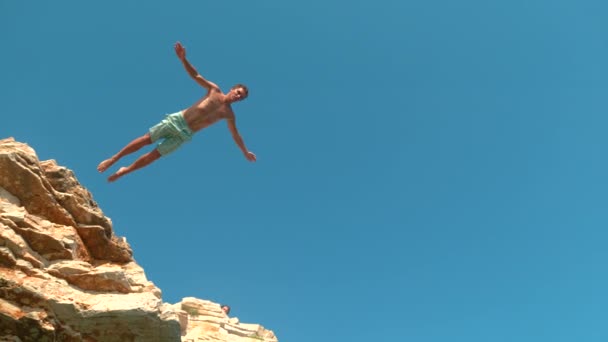 BOTTOM UP: Athletic tourist jumps off a cliff to dive into the refreshing ocean. — Stock Video