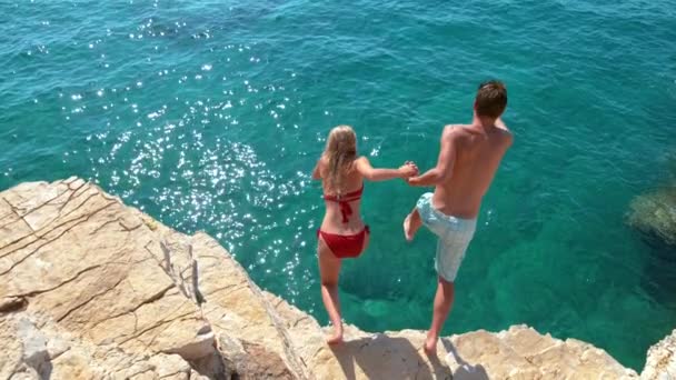 LOW MOTION: O casal de turistas decide saltar de um penhasco rochoso e mergulhar no mar . — Vídeo de Stock