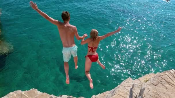 LOW MOTION: Turistas despreocupados de mãos dadas enquanto saltam para o mar refrescante — Vídeo de Stock