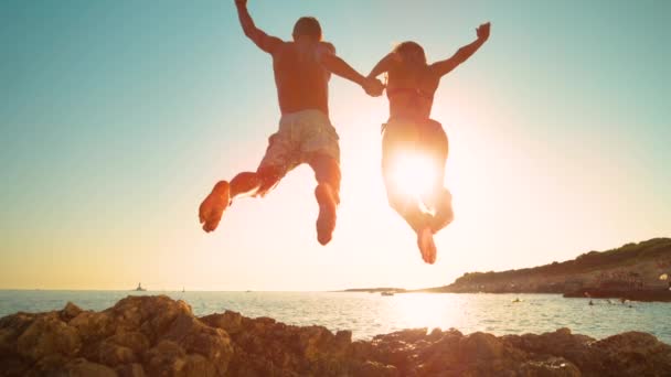 LENS FLARE: Carefree tourists hold hands while jumping into the refreshing sea — Stock Video