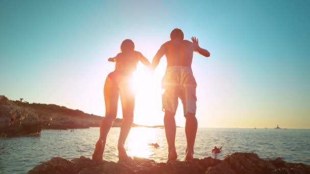 FLARE DE LOS LENTES: Los rayos dorados del sol brillan en pareja tomados de la mano mientras se sumergen en el mar. — Vídeos de Stock