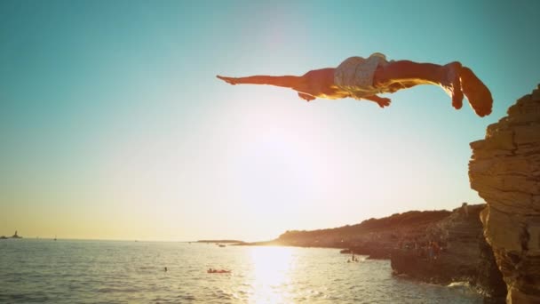 CLOSE UP: Sportlicher Mann stürzt bei Sonnenuntergang von einer Klippe kopfüber ins Meer — Stockvideo