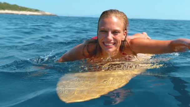 Ritratto: Allegro donna caucasica sdraiata sulla tavola da surf nuota verso la linea. — Video Stock