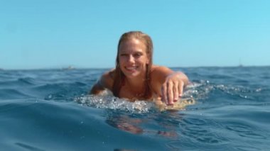 Gülümseyen sörfçü kız dalgaları yakalamak için çizgiye yüzerken eğleniyor..