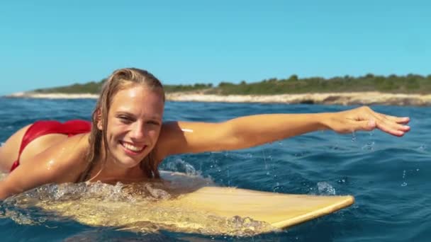 CLOSE UP: Pretty woman smiles while paddling out to line up on her surfboard. — Stock Video