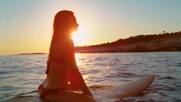 レンズフレア:豪華なサーファーの女の子は彼女のサーフボードに座って波を待っています. — ストック動画