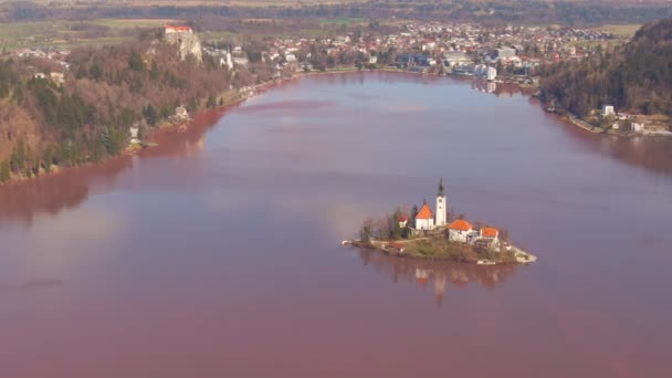 AERIAL: Fotografía cinematográfica de agua roja que rodea el hermoso islote del lago Bled — Vídeos de Stock