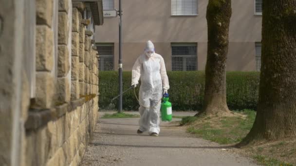 MOVIMIENTO Lento: La persona con un traje de materiales peligrosos blanco rocía la acera con desinfectante — Vídeos de Stock