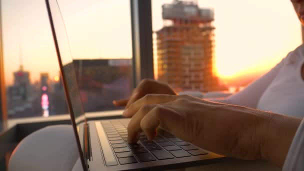 Bir kadın otel odasından altın güneş doğarken dizüstü bilgisayarıyla yazı yazıyor.. — Stok video