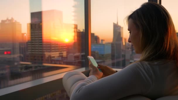 Sluiten omhoog: Jonge vrouw zit op de leren bank in haar hotelkamer bij zonsopgang. — Stockvideo