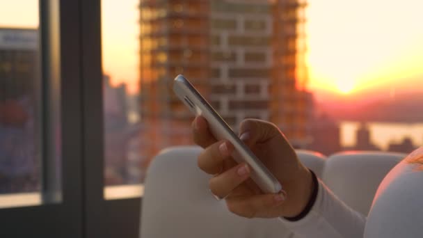 CLOSE UP: Неузнаваемая женщина плывет по экрану мобильного телефона на восходе солнца — стоковое видео