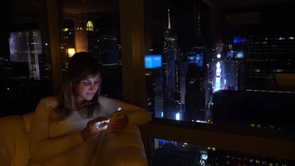 特写：年轻女人坐在皮革沙发上，用智能手机写一篇文章. — 图库视频影像