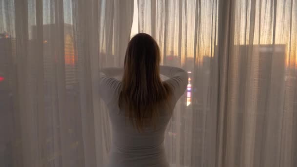 Movimiento lento: Mujer dibuja las cortinas y mira a Nueva York en la tarde soleada . — Vídeos de Stock